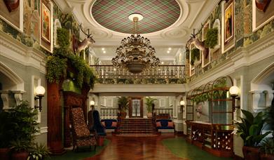 Grand lobby of Slieve Donard with dark wooden floors, lots of greenery and a large chandelier.