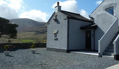 A large grey farmhouse with an exterior staircase in the mountains.