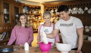 Male and female couple at kitchen table with Tracey.  The male is pouring baking flour from bag into a bowl.