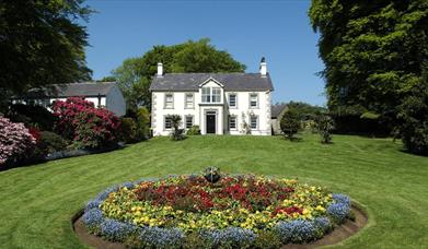 A house at the end of a lawn with a large circular flowerbed.