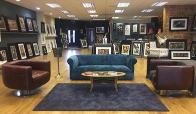 Photo of the inside of the gallery showing seating area and paintings on display for sale