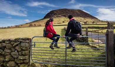 A couple of hikers sitting on a gate admiring the view of Slemish in the background