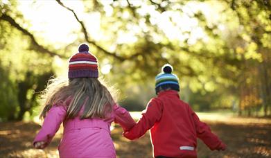 Photo of two children with woolly hats on running through the autumn leaves of the park