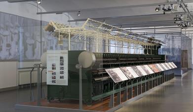 A large old spinning frame exhibit behind glass with information displays.