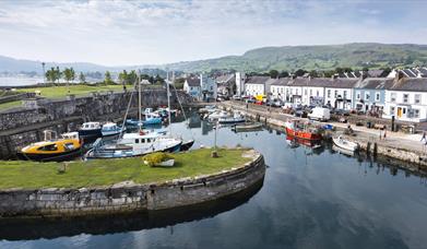 Aerial view of Carnlough Harbour with shops and homes in the background and boats in the harbour