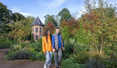 A couple walking on a garden path with lots of trees and other plants.