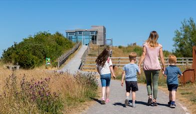 Three children walking with a woman towards the Limekiln Observatory - a glass building on a hill.