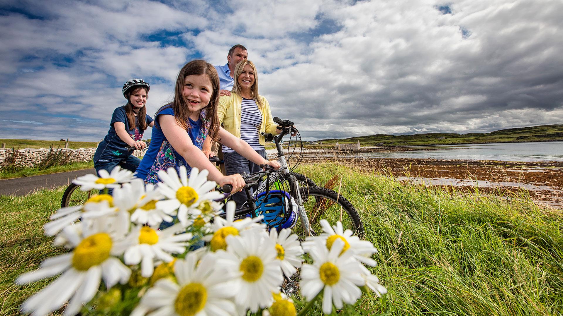 Family on bicycles enjoying the sunshine on Rathlin Island with daisies at the forefront of the image