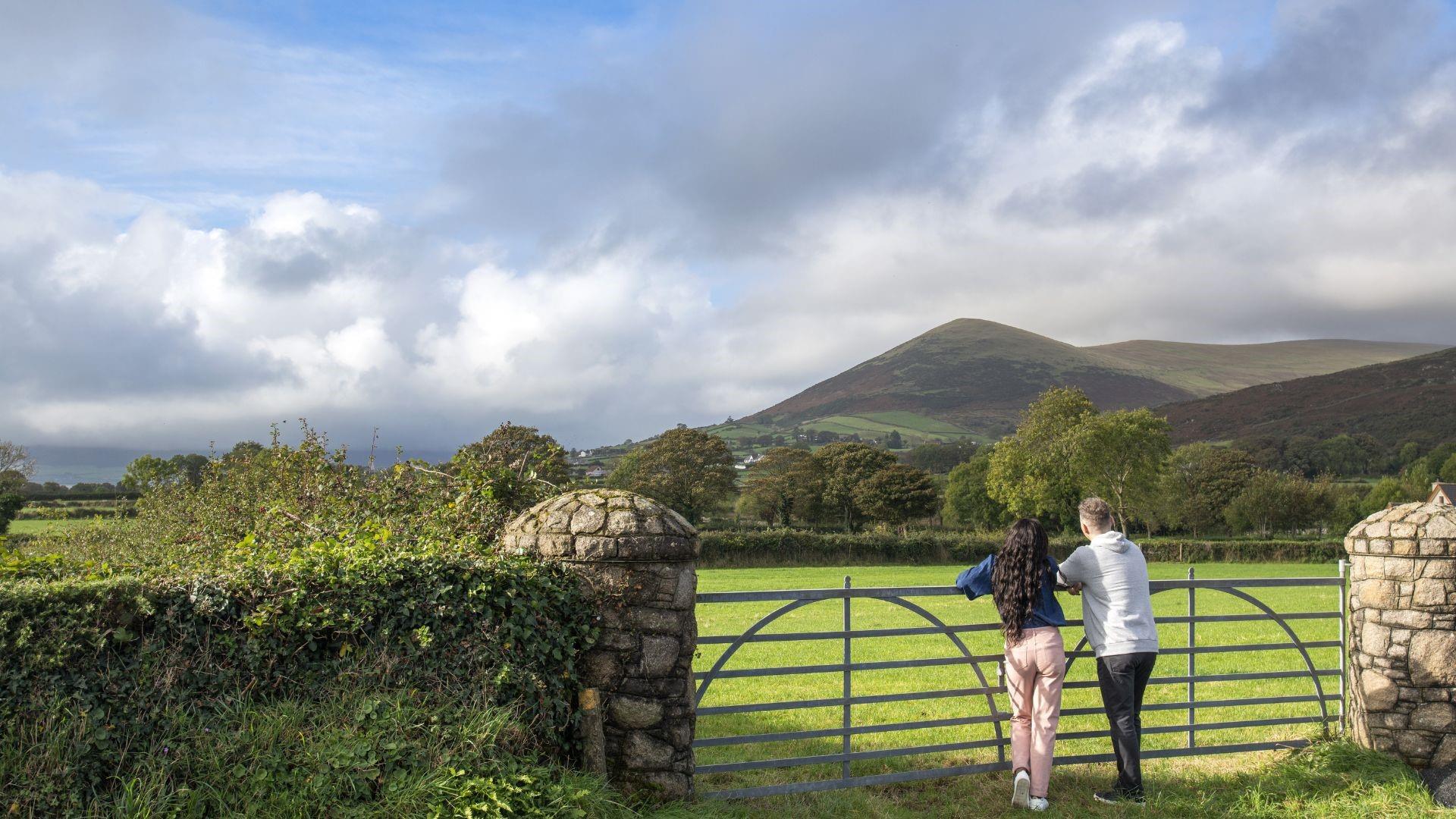 Couple standing at a gate admiring the lush green countryside and mountain in the distance