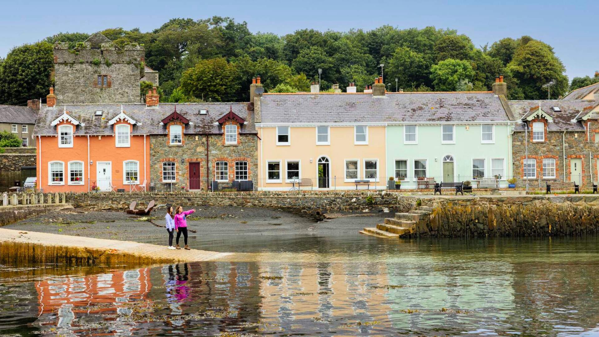Two women look out over the lough at Strangford, with colourful houses in the background