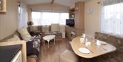 The main area of the caravan featuring a dining table, TV and wrap around sofa