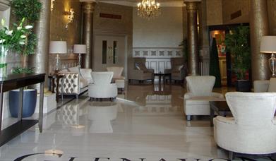 Image of the entrance hall with shiny tiled floors, cream armchairs, gold metallic columns and patterned wallpaper 