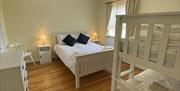 Spacious family room which white wooden double bed and bunk beds,  Bedside cabinet, chair and chest of drawers in matching white wood.