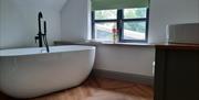image of free standing bath beside window with wash basin and vanity unit