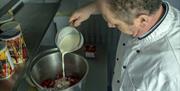 Man pouring milk into container with strawberries to make ice-cream.