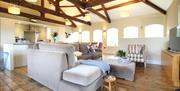 Image shows large lounge with corner sofa, chair, wooden floor. TV and wooden beams