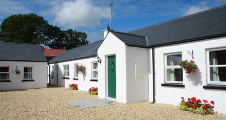 Image shows front of whitewashed property with green door and gravel drive. Flowerbeds on gravel outside windows