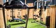 Image shows small gym area with bench and weights, running machine
