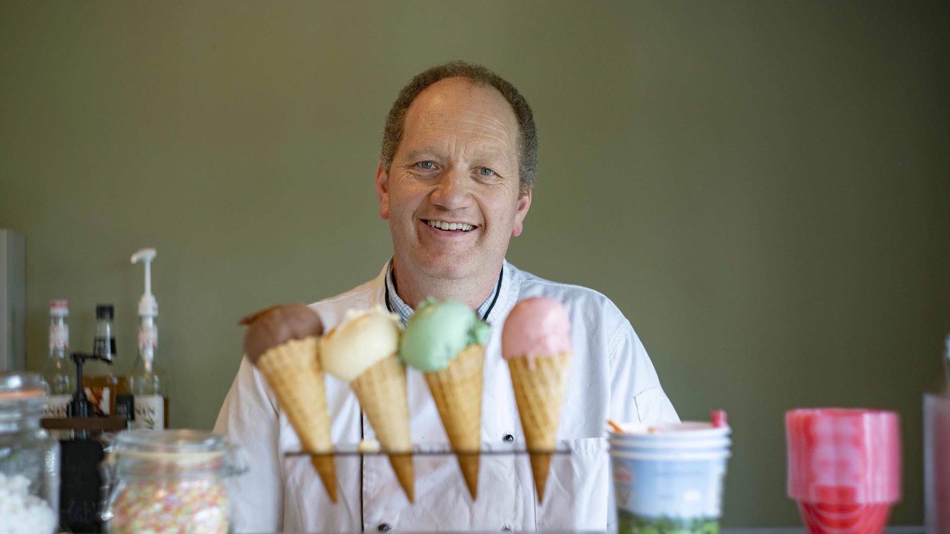 Man smiling standing in front of 4 different ice-creams.