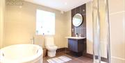 Image shows large bathroom with round bath, separate shower, toilet and sink with mirror above