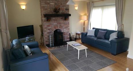 Image shows lounge area with 2 sofas, fireplace and wooden floor