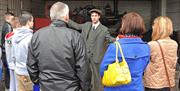 Photo of a gent dressed in old fashioned clothing giving a talk to a group of visitors to the museum