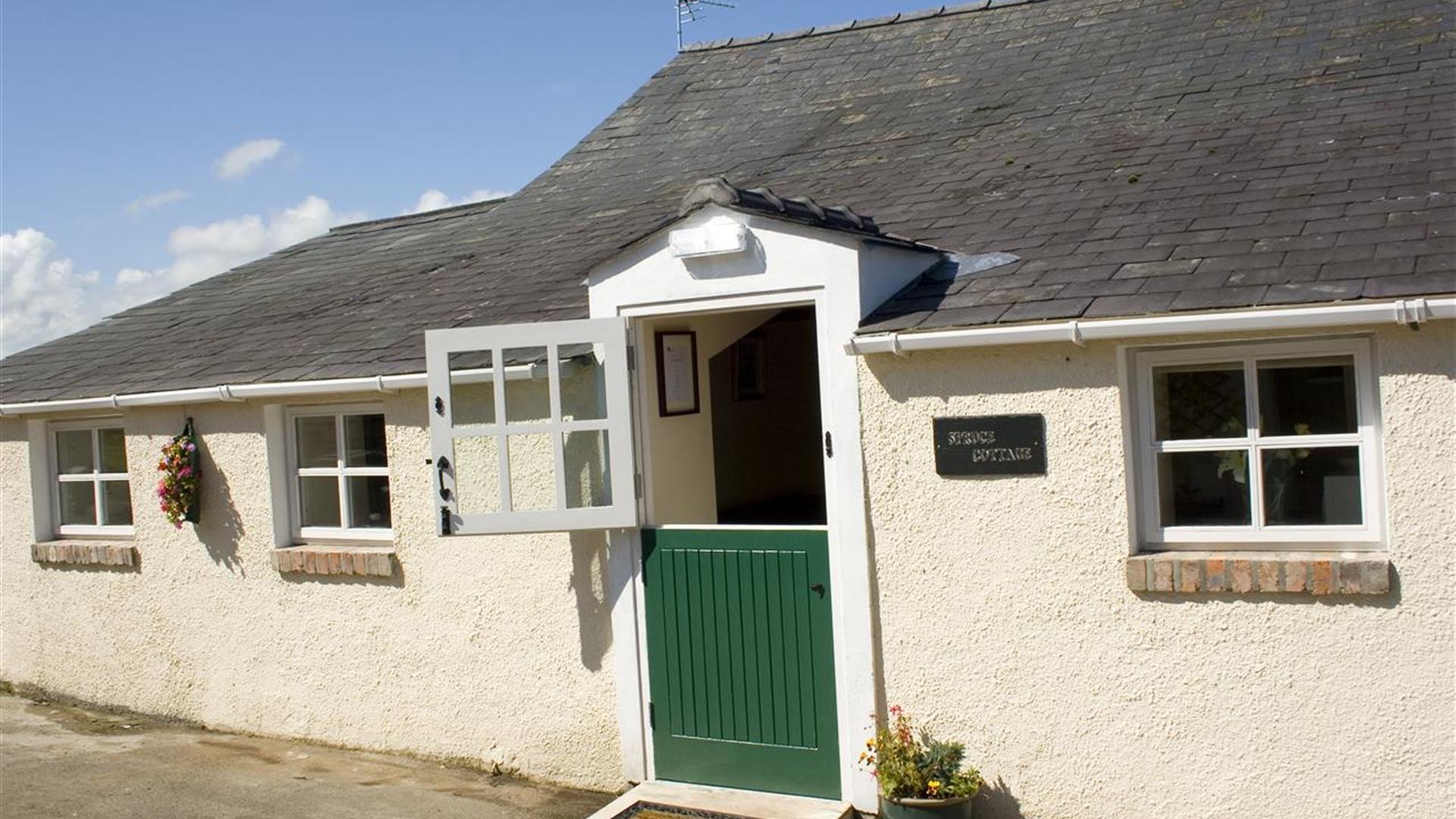 Image shows front of cottage with green stable door as entrance