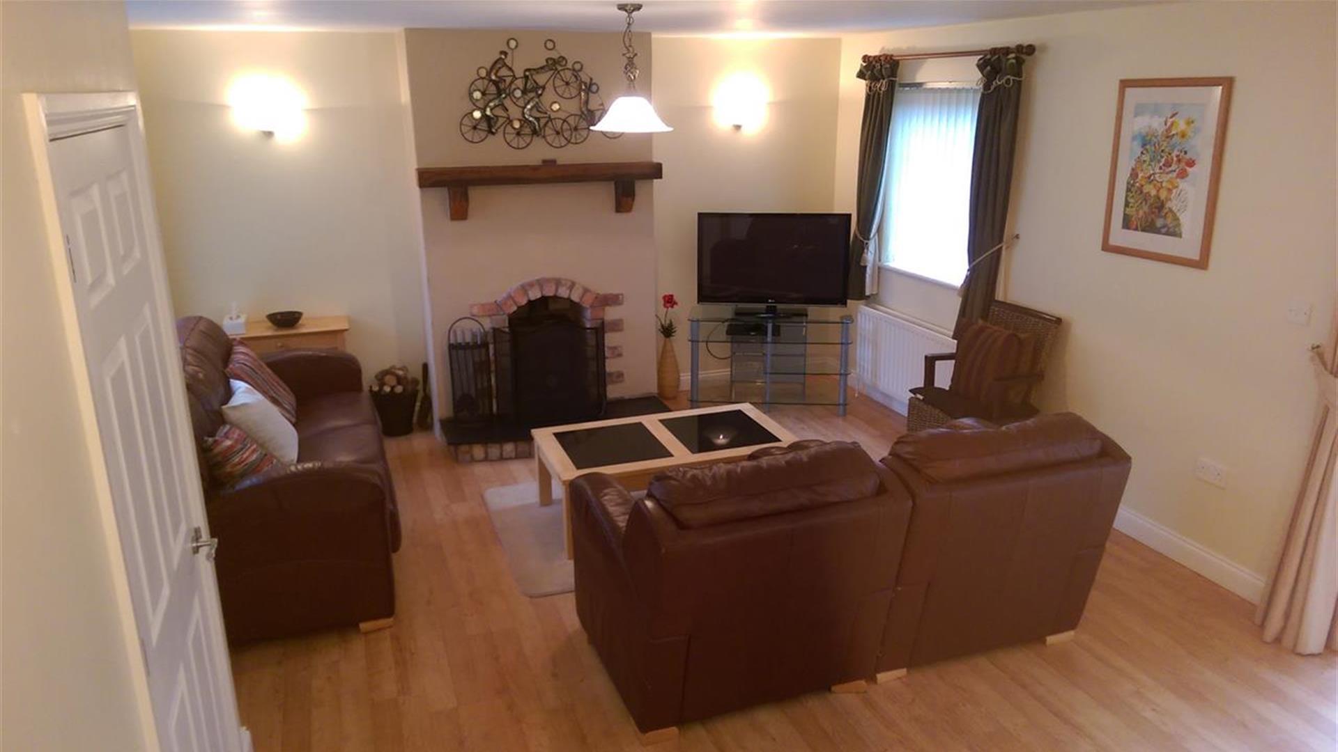 Image shows lounge area with 2 sofas, fireplace and TV