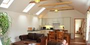 Image shows lounge and kitchen/dining area with leather sofas, high ceiling, dining table and chairs