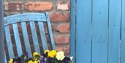Image shows blue wooden fence and blue wooden chair with flowers in flower bed