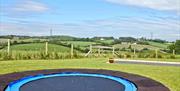 Image shows a large trampoline in a field with extensive views of the countryside
