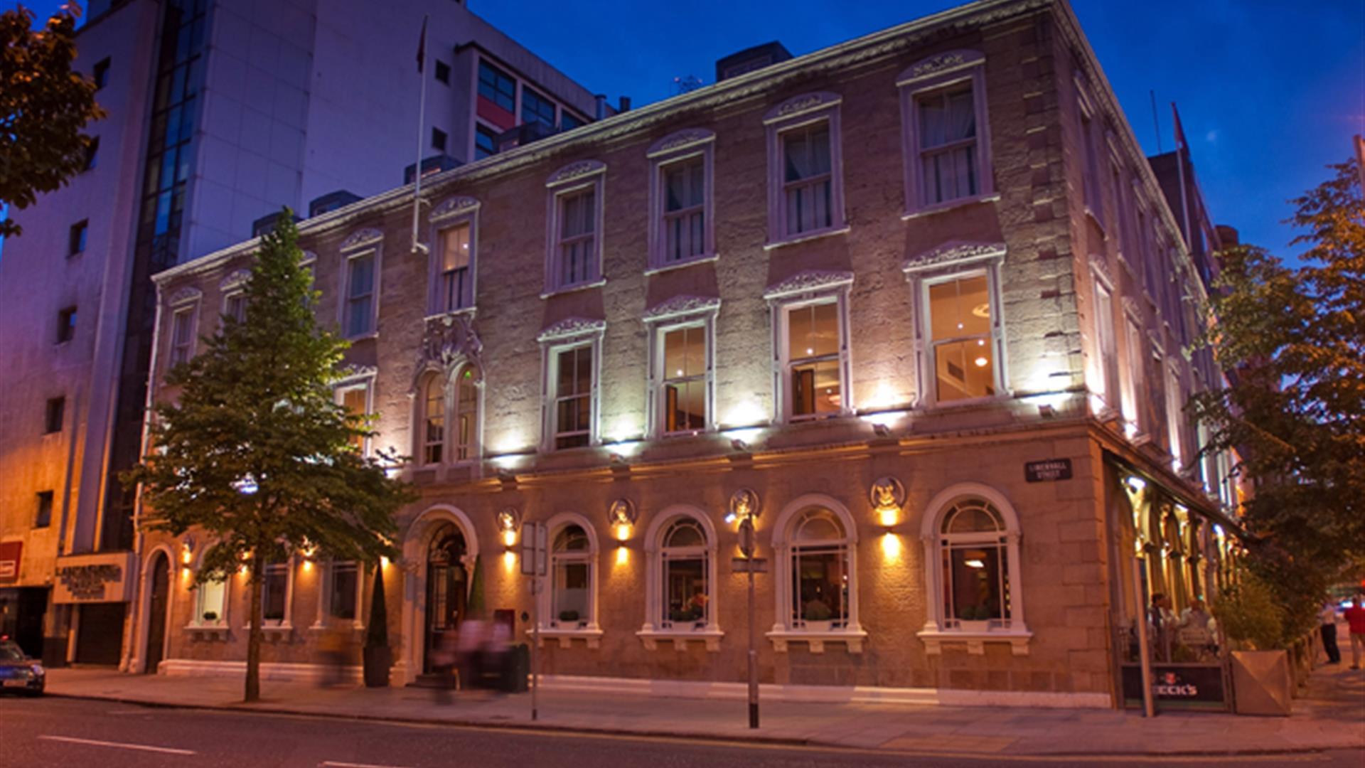 Exterior view of a three-story city hotel, lit at night with a tree. Exterior view of a three-story city hotel, lit at night with a tree.