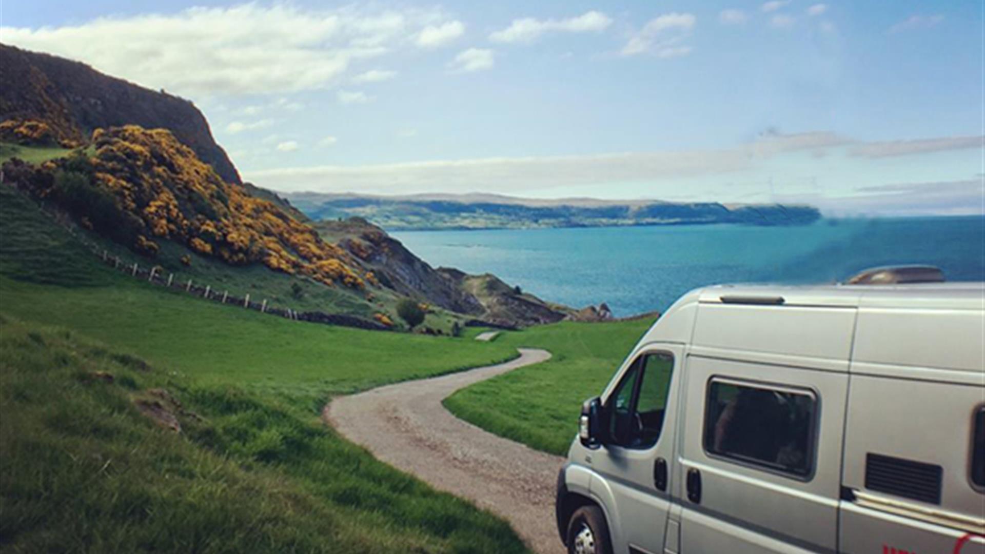 Image shows campervan on road leading down to the sea