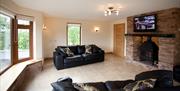 living area with large windows, 2 black 2 seater sofas, brick fireplace, stove and TV