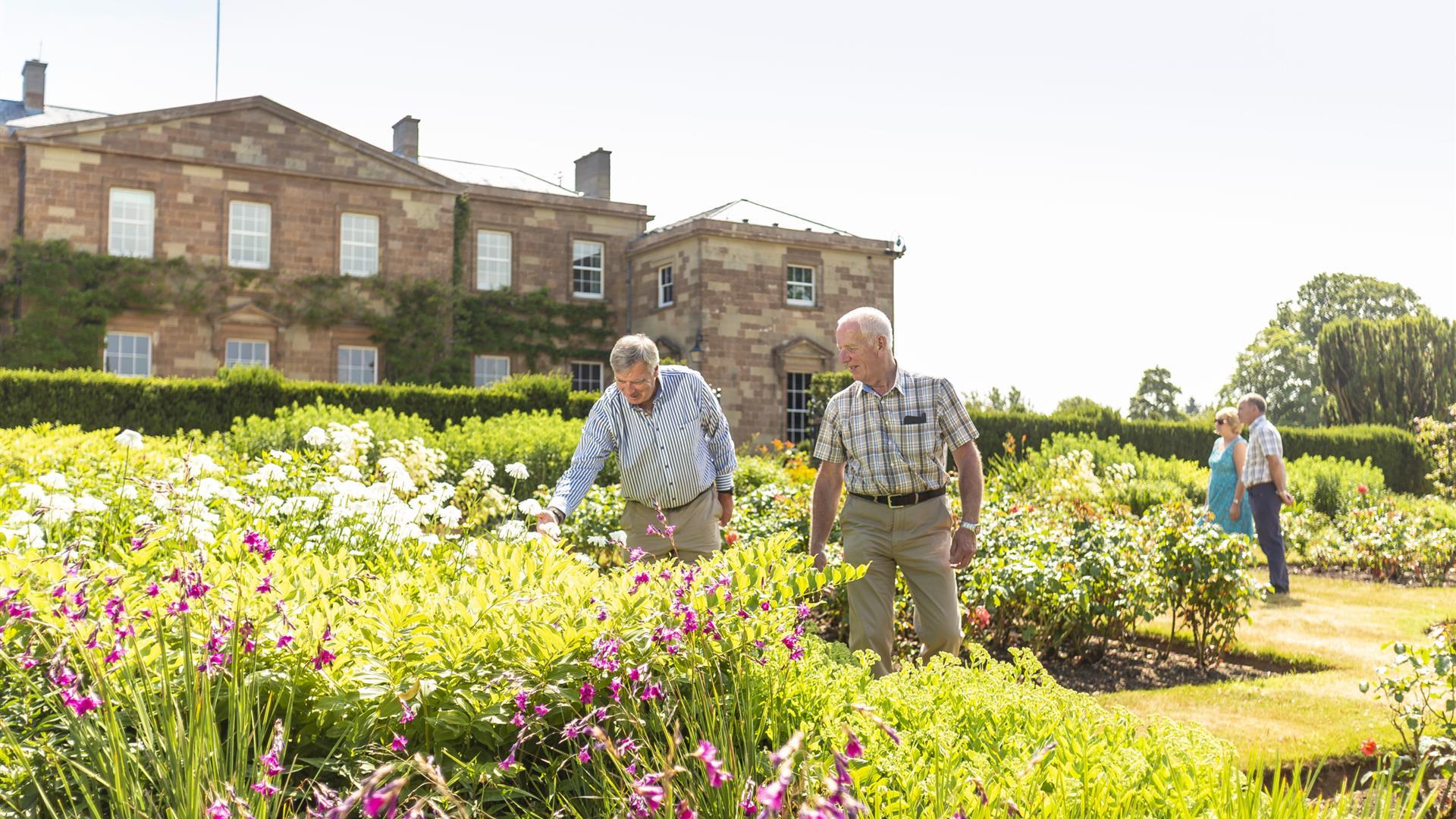 image is of visitors enjoying the gardens and inspecting the flowers and plants with the castle in the background