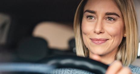 A smiling woman with her hands on the steering wheel of a car.
