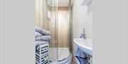 Corner shower with sink and decorated with nautical blue and white stripped towels and storage unit.