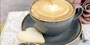 Close up image of a full coffee cup with heart shaped shortbread on saucer