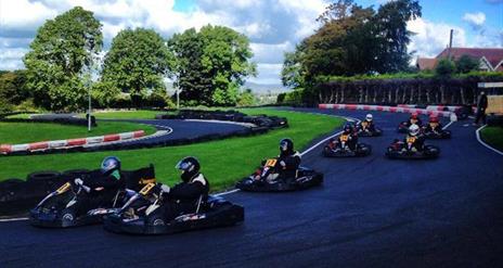 Image is of various people racing go-karts on an outdoor track