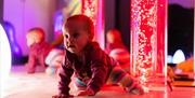 Baby girl crawling in sensory rooms at High Rise Lisburn with bubble tubes behind her