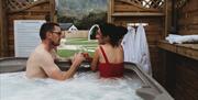 Couple in Hot Tub looking out to scenic view and glamping pods