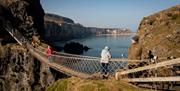 People cross carrick-a-rede rope bridge with Mark Rodgers of Dalriada Kingdom Tours guiding them