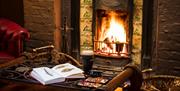 a table with a book on fishing and a pint of Guinness sits infront of a lit fireplace