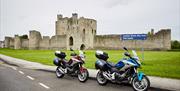 Image shows 2 motorcycles parked on road outside a castle