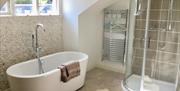 Image shows stand alone bath with tall radiator and shower cubical. Small window above bath