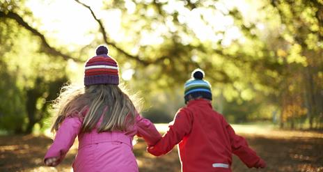 Photo of two children with woolly hats on running through the autumn leaves of the park