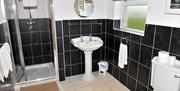 Image shows bathroom with walk in shower, sink and toilet. Tiled floor.