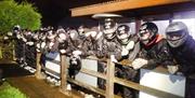 Image is of many riders with helmets on leaning over a fence