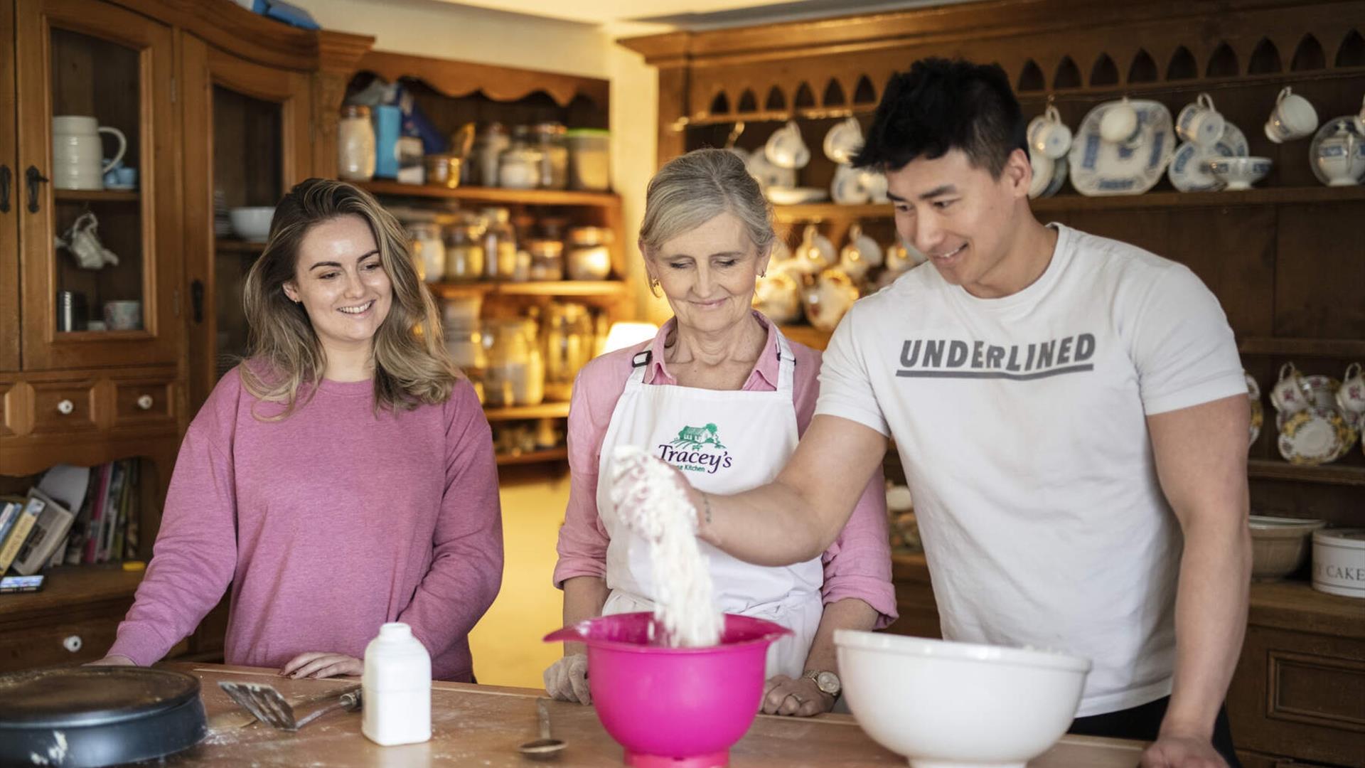 Male and female couple at kitchen table with Tracey.  The male is pouring baking flour from bag into a bowl.