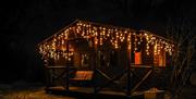 Exterior image of the rustic wooden cabin at night, the veranda dripping with fairy lights